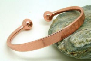 A pure copper torque bracelet with a flattened top tapering down to two copper balls each containing a rare earth magnet